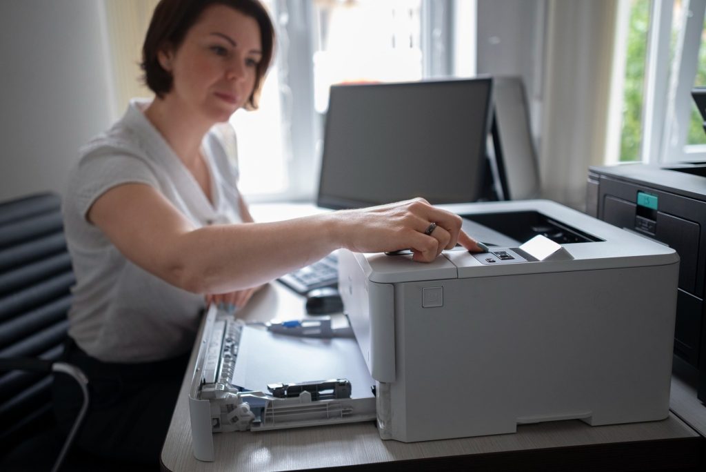 A woman is sitting at a desk in an office, adjusting a printer